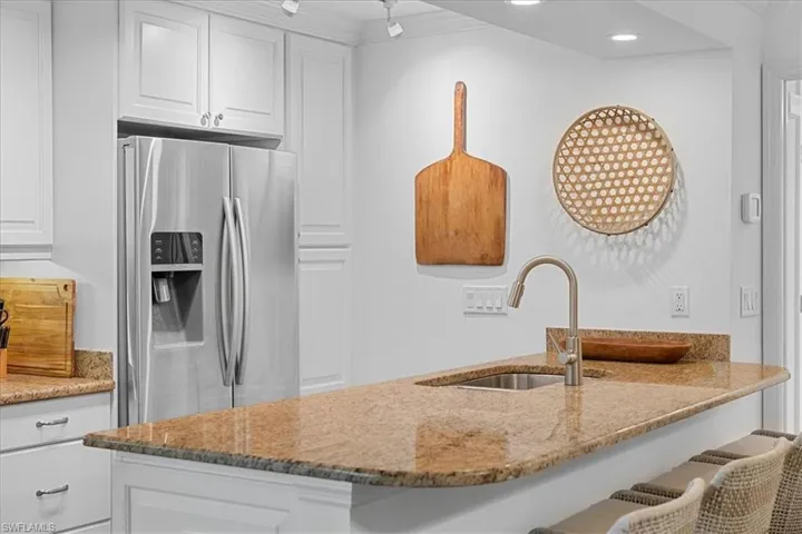 Kitchen with white cabinets, stainless steel refrigerator with ice dispenser, light stone countertops, and a sink
