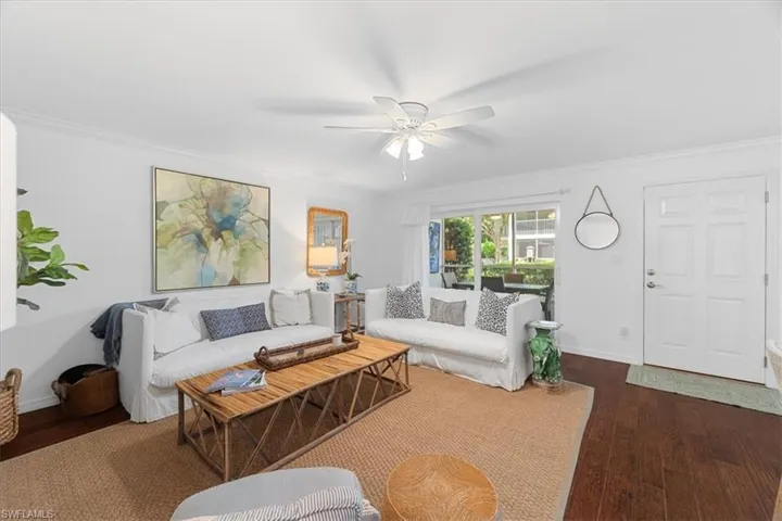 Living room with dark wood-type flooring, ceiling fan, baseboards, and ornamental molding