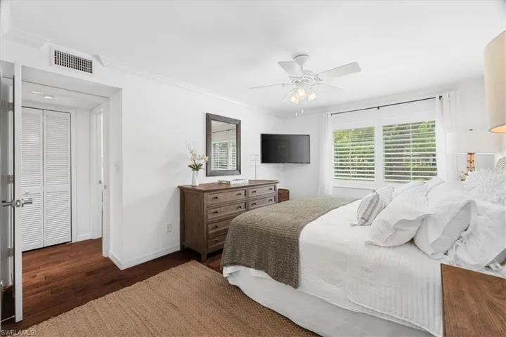 Bedroom featuring baseboards, visible vents, a ceiling fan, wood finished floors, and ornamental molding
