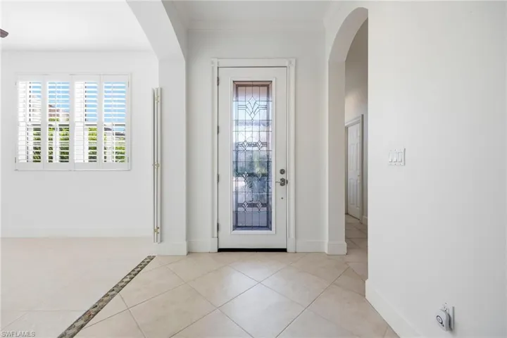 Entryway with arched walkways, light tile patterned floors, and ornamental molding