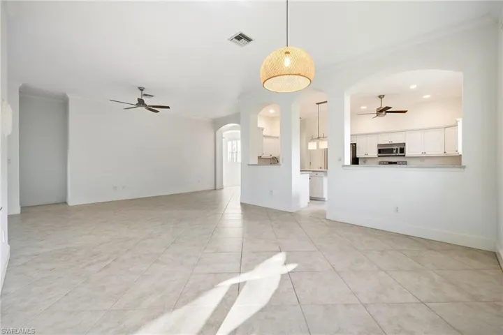 Unfurnished living room featuring ceiling fan, arched walkways, ornamental molding, light tile patterned floors, and recessed lighting