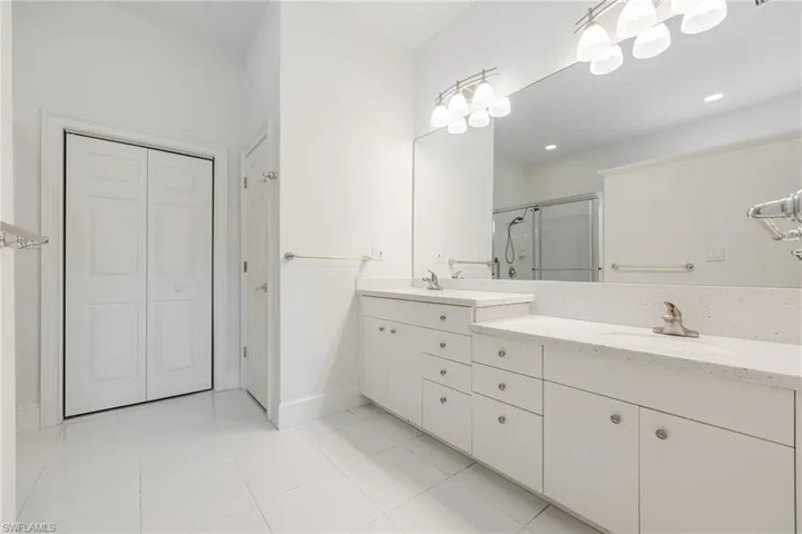 Full bathroom featuring double vanity, a closet, a stall shower, and light tile patterned floors