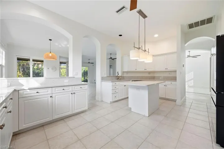 Kitchen featuring white cabinets, a ceiling fan, arched walkways, and a kitchen island