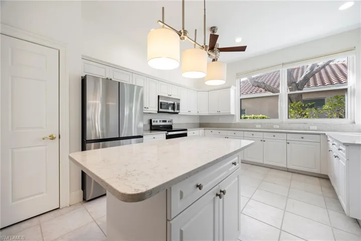 Kitchen featuring stainless steel appliances, white cabinets, a kitchen island, light stone counters, and pendant lighting