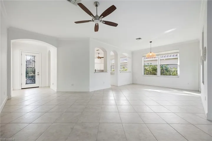 Unfurnished room featuring arched walkways, ornamental molding, ceiling fan, light tile patterned floors, and healthy amount of natural light