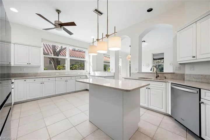 Kitchen with a center island, white cabinets, a ceiling fan, light stone countertops, and stainless steel appliances