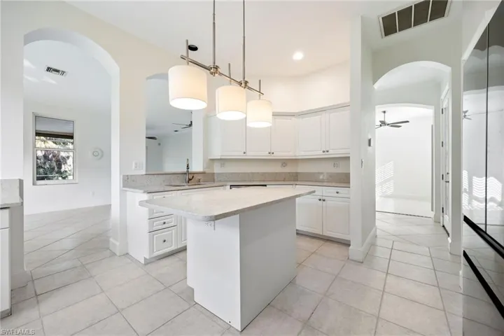 Kitchen featuring ceiling fan, arched walkways, white cabinets, a kitchen island, and light tile patterned floors