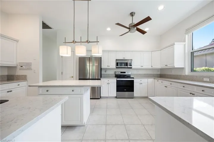 Kitchen featuring stainless steel appliances, light stone countertops, white cabinetry, and pendant lighting