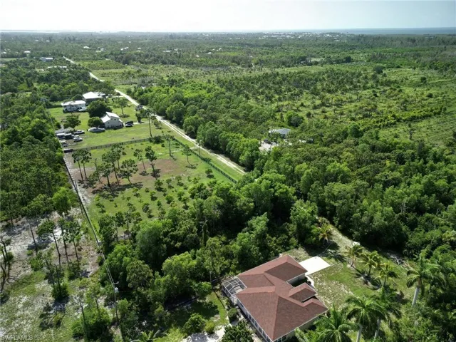 Aerial perspective showcasing extensive acreage with mature trees and a residential structure featuring a hip roof