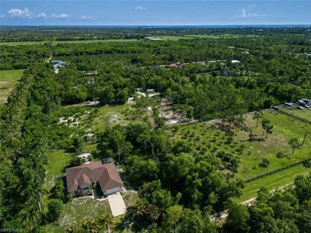 Single-story residence set amidst expansive green acreage, featuring a brown shingle roof, attached garage, and a concrete driveway