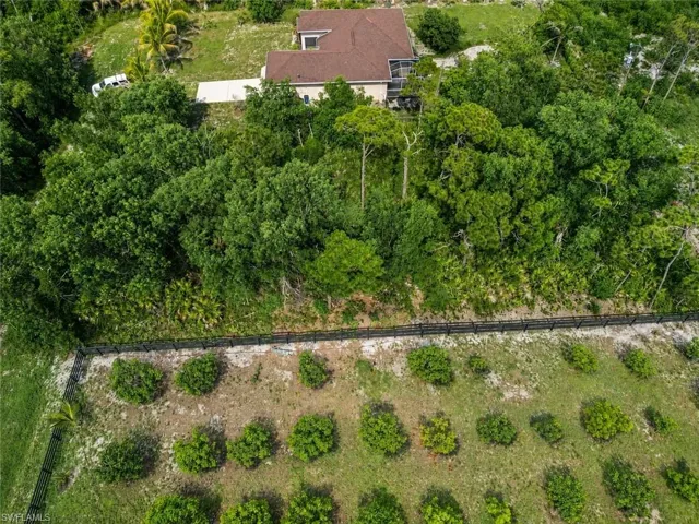 Aerial perspective showcasing a property with a brown-roofed residence, extensive surrounding foliage, a paved driveway, and a fenced perimeter