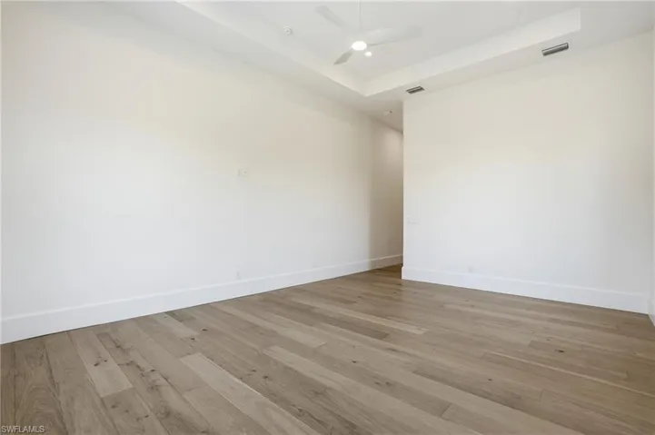 Unfurnished room featuring a tray ceiling, hardwood / wood-style floors, and ceiling fan