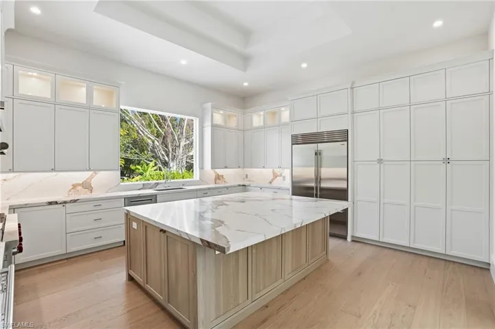 Kitchen featuring dual tone cabinetry, recessed lighting, light stone counters, light wood-style flooring, and high quality appliances