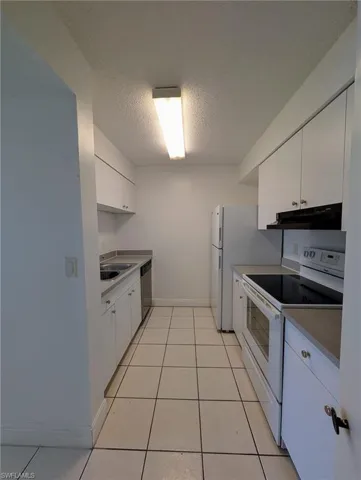 Kitchen featuring white appliances, white cabinets, a textured ceiling, light tile patterned floors, and under cabinet range hood