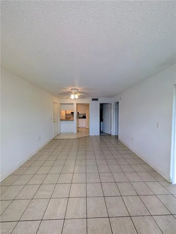 Unfurnished living room featuring a textured ceiling, ceiling fan, and light tile patterned floors