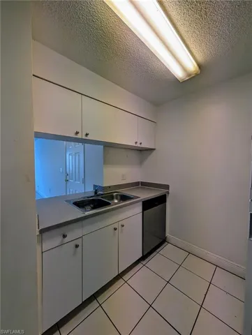 Kitchen featuring white cabinetry, light tile patterned flooring, dishwasher, and a textured ceiling