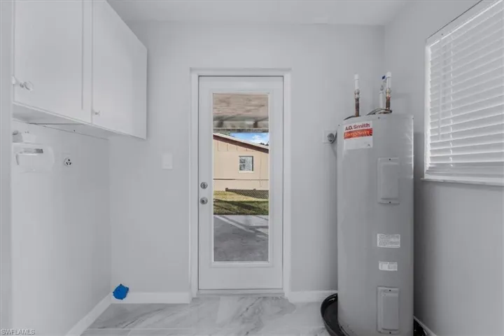 Washroom featuring hookup for an electric dryer, electric water heater, light marble finish flooring, cabinet space, and plenty of natural light