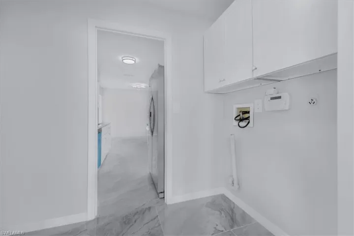 Washroom featuring washer hookup, light marble finish floors, and cabinet space