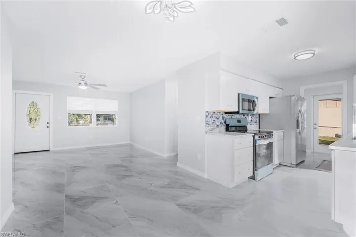 Kitchen featuring appliances with stainless steel finishes, white cabinetry, light marble finish flooring, tasteful backsplash, and open floor plan