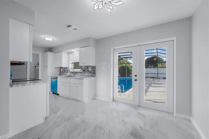 Kitchen with light marble finish flooring, french doors, tasteful backsplash, white cabinetry, and dishwashing machine