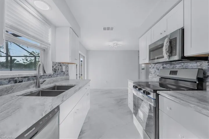 Kitchen with stainless steel appliances, decorative backsplash, white cabinets, and light marble finish floors