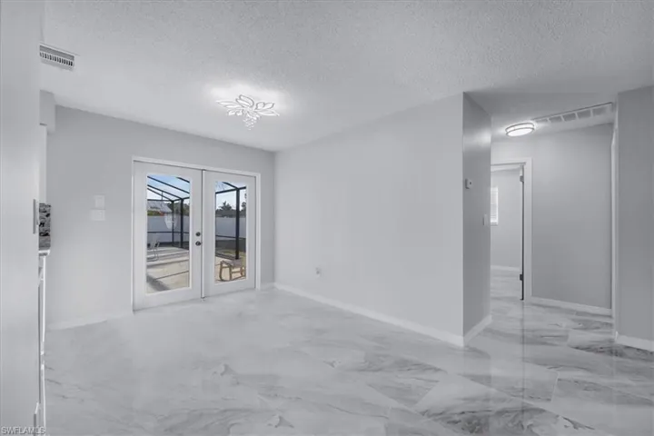 Unfurnished room with a textured ceiling, light marble finish floors, and french doors