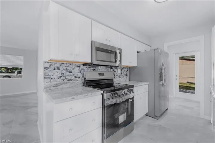 Kitchen with appliances with stainless steel finishes, white cabinetry, light marble finish flooring, and tasteful backsplash