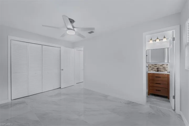 Unfurnished bedroom with light marble finish flooring, connected bathroom, ceiling fan, and a closet