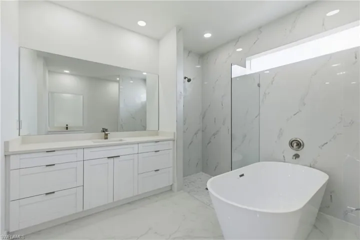 Bathroom featuring stone wall, vanity, a marble finish shower, a freestanding tub, and recessed lighting