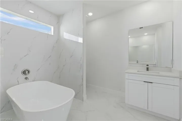 Full bath featuring a freestanding tub, vanity, recessed lighting, stone wall, and light marble finish flooring