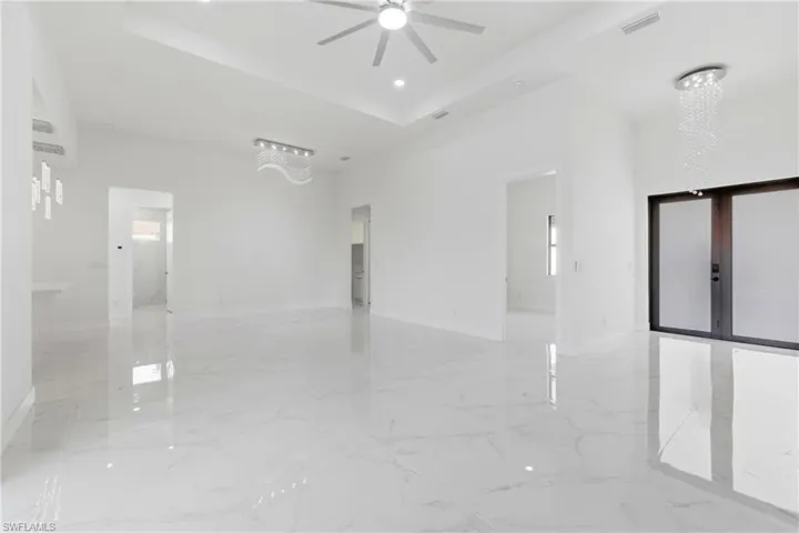 Empty room with suspended lighting, a ceiling fan, a high tray ceiling, and light marble finish floors