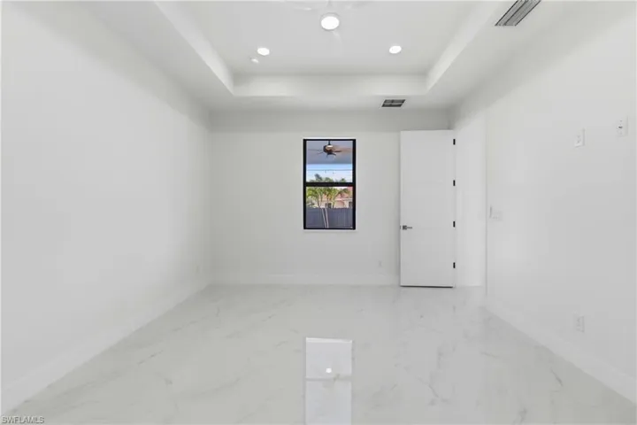 Spare room with a raised ceiling, light marble finish floors, and recessed lighting