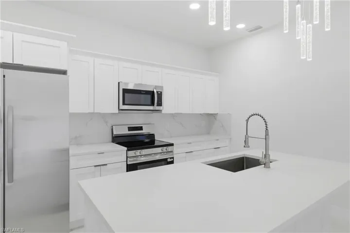 Kitchen featuring stainless steel appliances, white cabinetry, a center island with sink, and light stone countertops