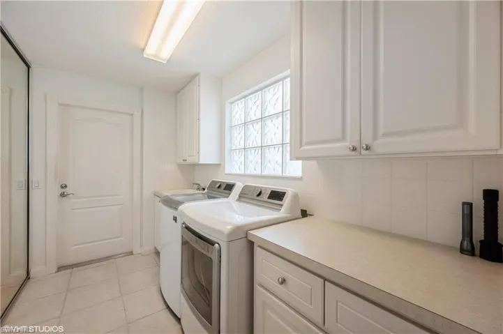 Laundry room with light tile patterned flooring, washing machine and dryer, baseboards, and cabinet space