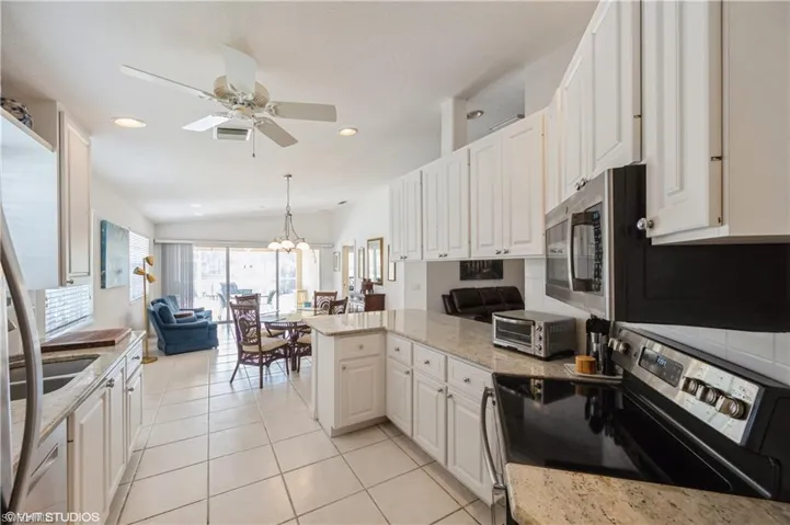 Kitchen featuring white cabinets, a peninsula, electric stove, and ceiling fan with notable chandelier