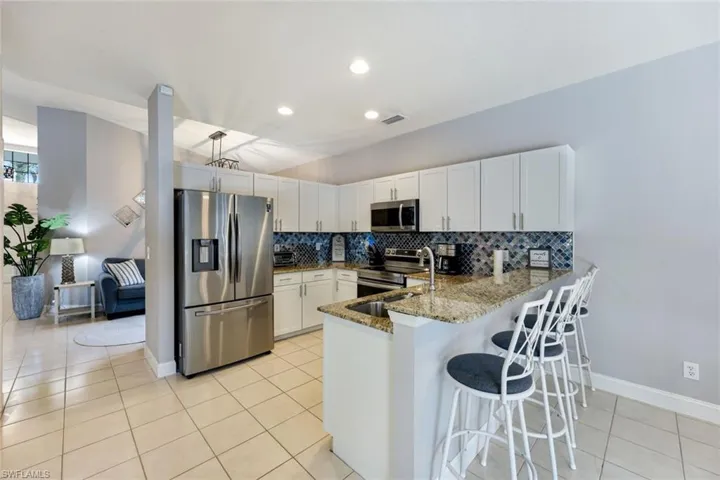 Kitchen featuring stainless steel appliances, a peninsula, tasteful backsplash, stone countertops, and light tile patterned floors
