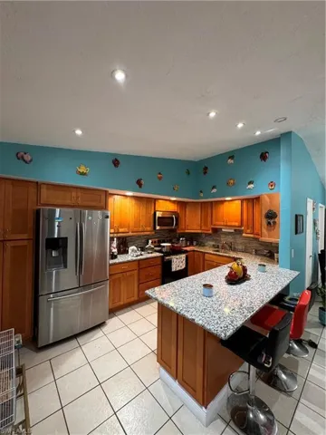 Kitchen featuring a kitchen breakfast bar, light tile patterned floors, fridge, range, and tasteful backsplash