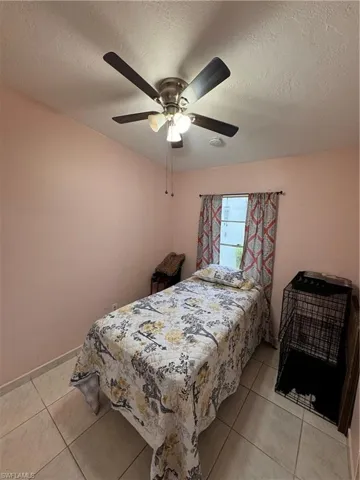 Bedroom featuring ceiling fan, light tile patterned flooring, and a textured ceiling