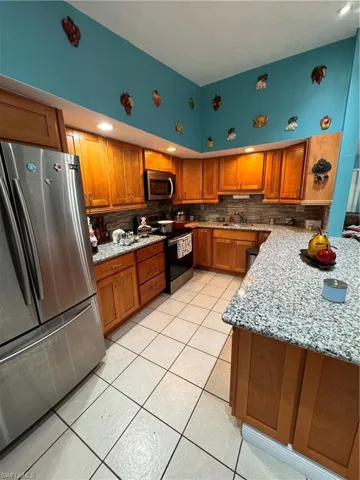 Kitchen with backsplash, sink, refrigerator, light stone counters, and electric range