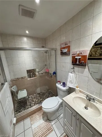 Bathroom featuring a shower with door, toilet, tile patterned floors, tile walls, and vanity