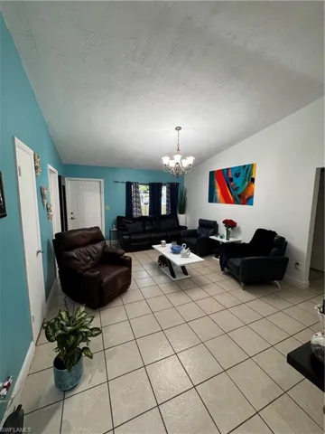 Tiled living room with a notable chandelier, vaulted ceiling, and a textured ceiling