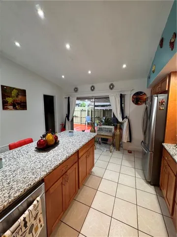 Kitchen with light stone counters, dishwashing machine, light tile patterned floors, vaulted ceiling, and refrigerator