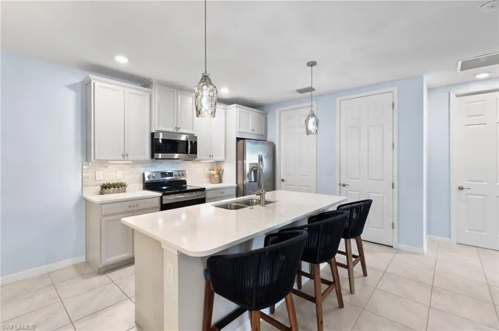 Kitchen featuring stainless steel appliances, a breakfast bar area, a center island with sink, hanging light fixtures, and backsplash