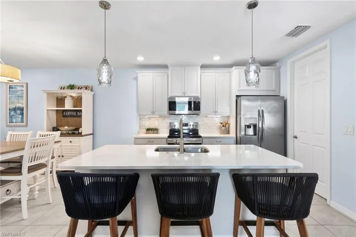 Kitchen featuring a kitchen bar, stainless steel appliances, a center island with sink, white cabinetry, and light tile patterned flooring