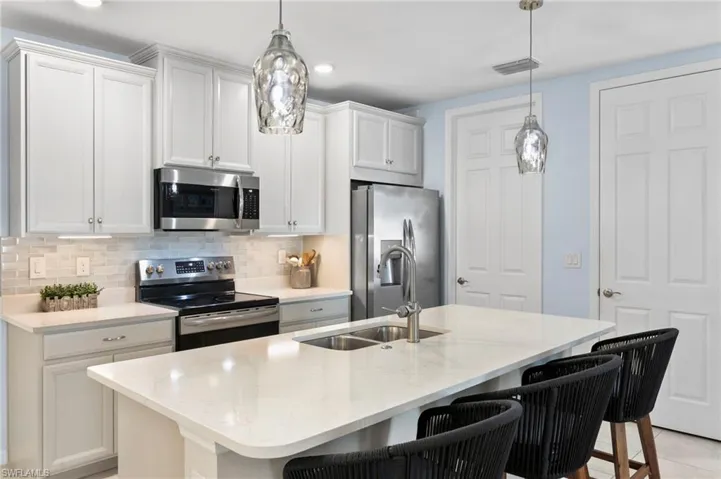 Kitchen featuring stainless steel appliances, a kitchen bar, a kitchen island with sink, light stone countertops, and white cabinets