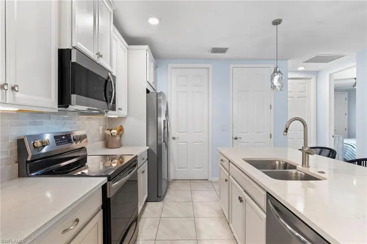Kitchen featuring stainless steel appliances, white cabinetry, light stone counters, and decorative light fixtures