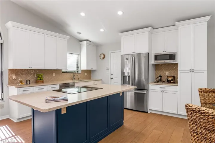 Dual tone kitchen with stainless steel appliances, light wood-style floors, light stone counters, lofted ceiling, and recessed lighting
