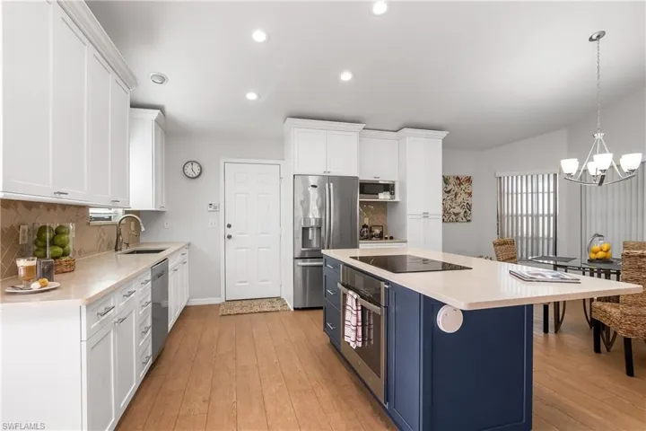 Kitchen featuring two tone cabinets, stainless steel appliances, light wood-style floors, light stone countertops, and tasteful backsplash