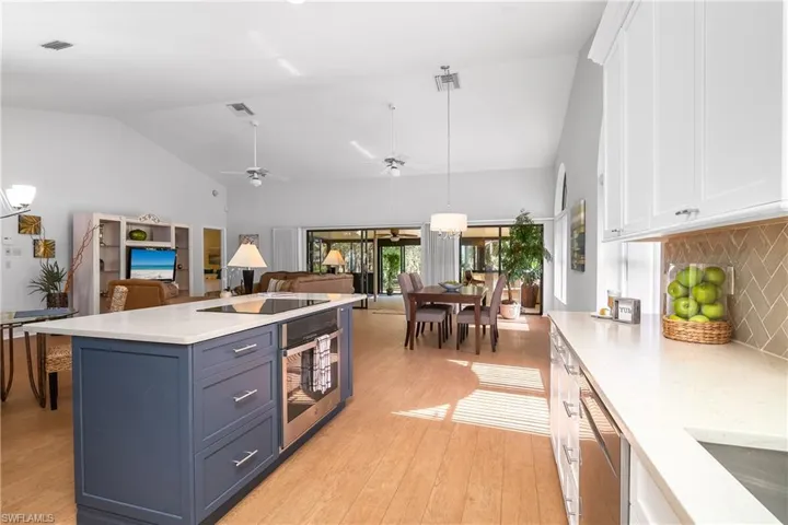 Dual tone kitchen with hanging light fixtures, lofted ceiling, ceiling fan, stainless steel appliances, and light stone counters