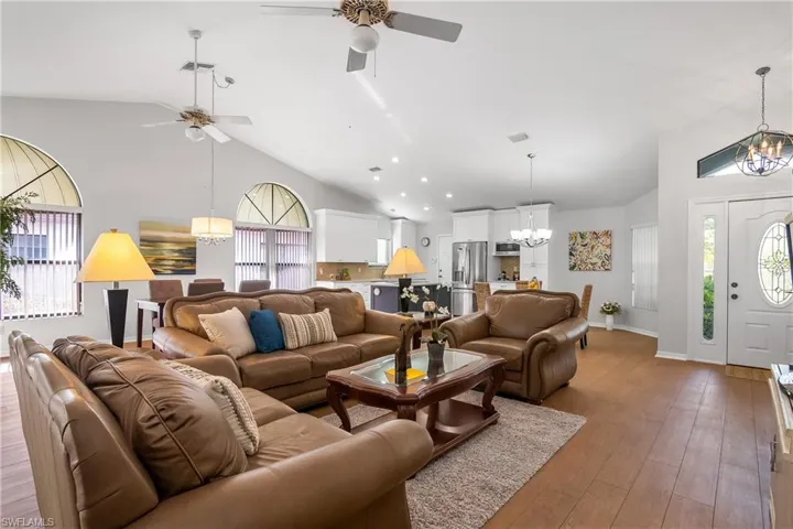 Living room featuring hanging lights, lofted ceiling, wood-type flooring, and a ceiling fan